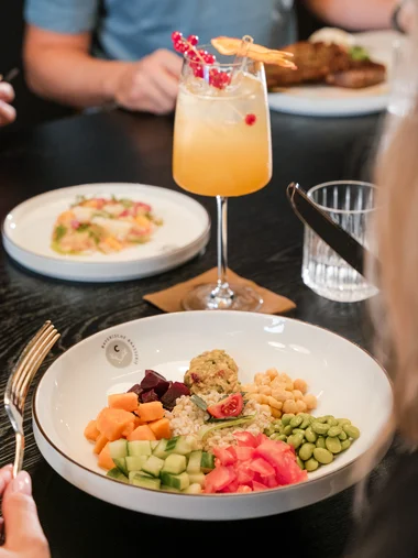 Bunte Gemüsepflaster und Hummus auf Teller mit Cocktail im Hintergrund