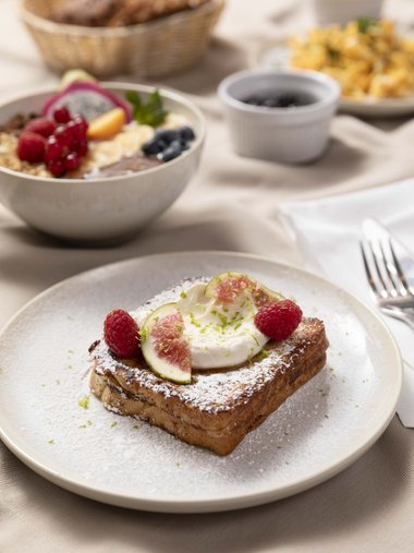 Französischer Toast mit Sahne, Feigen und Himbeeren auf weißem Teller.