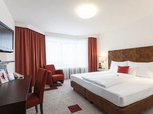 Modernes Hotelzimmer mit großem Bett, rotem Sessel, Schreibtisch und Fernseher