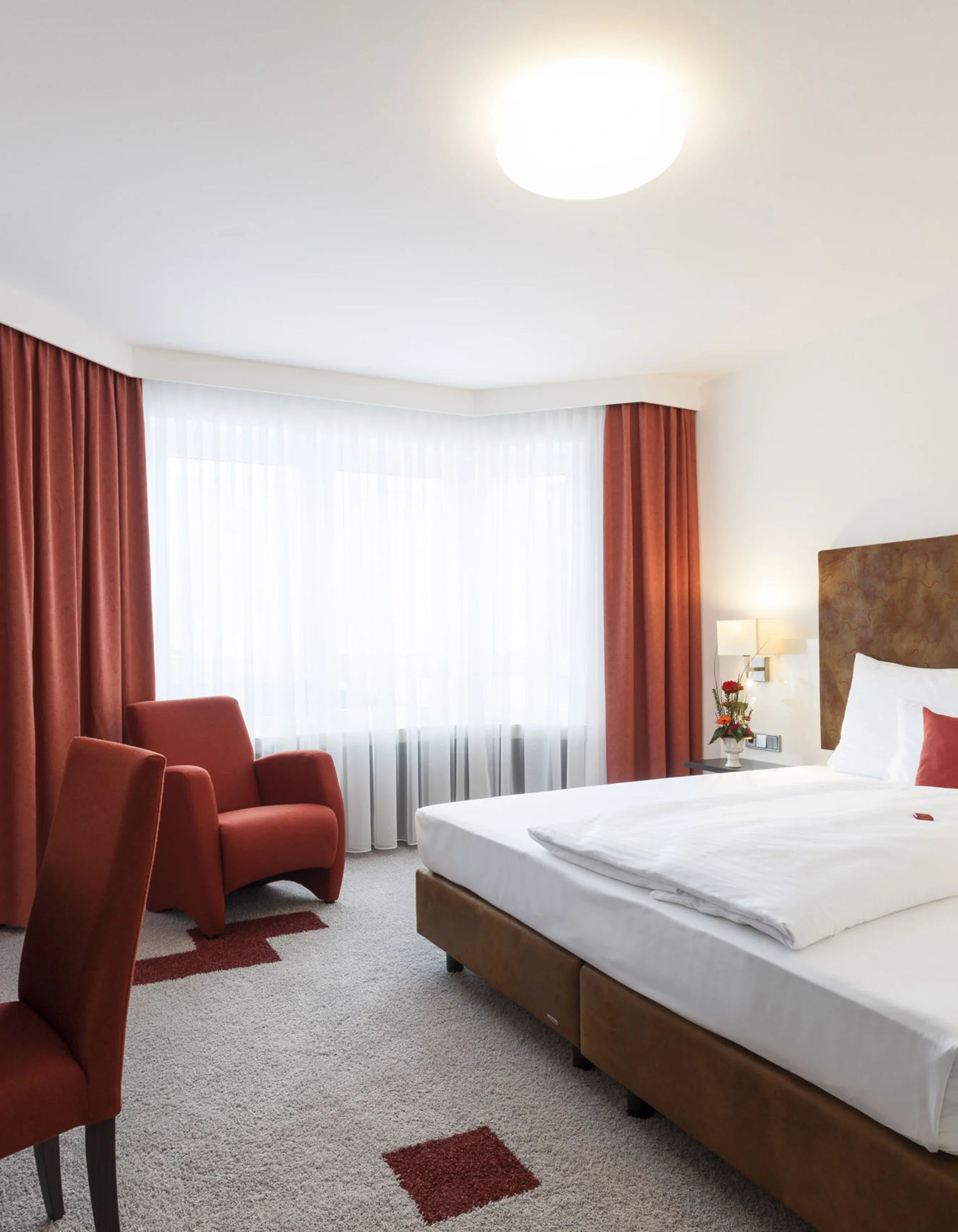 Modernes Hotelzimmer mit großem Bett, rotem Sessel, Schreibtisch und Fernseher