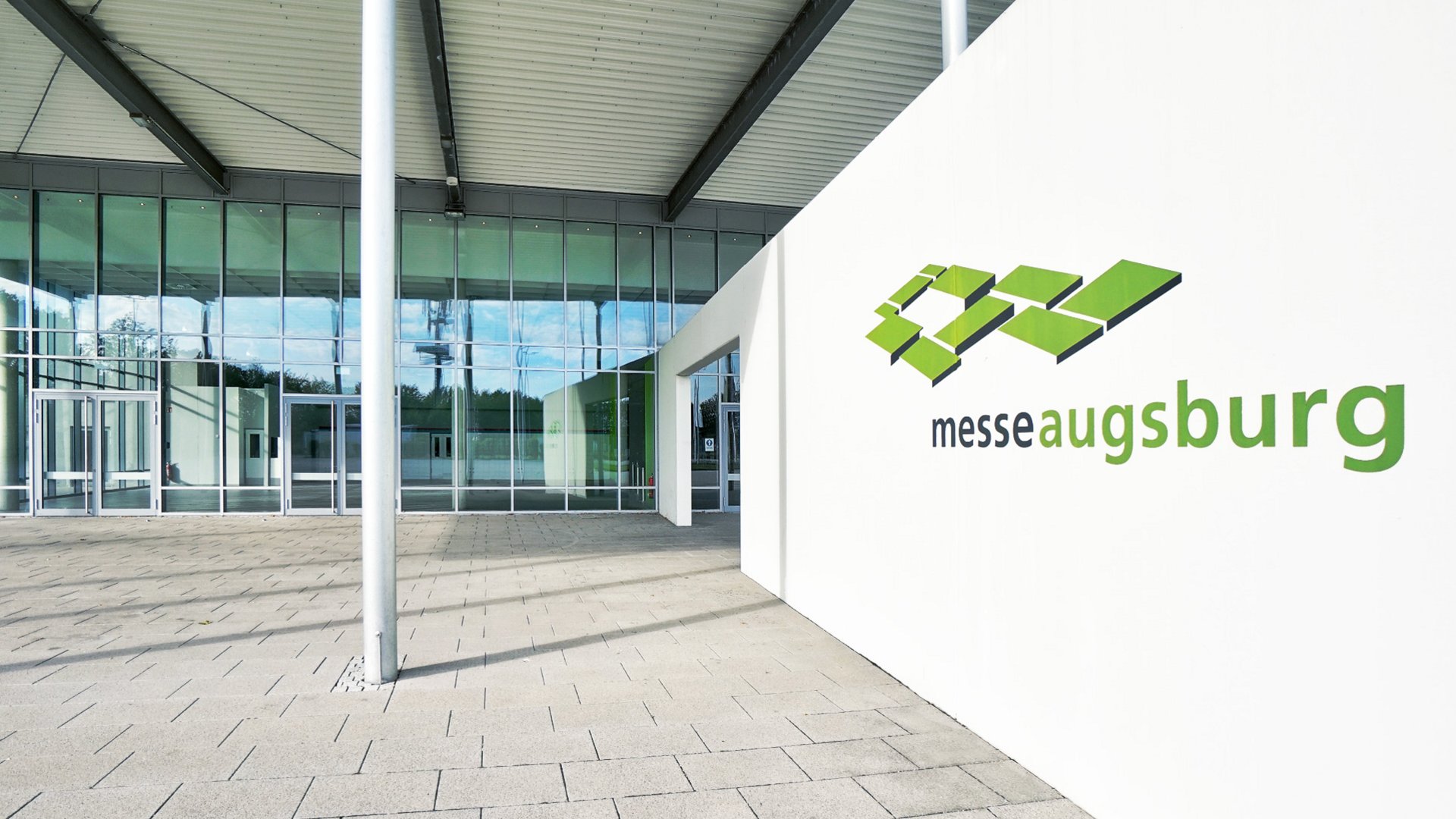 Eingang der Messe Augsburg mit grünem Logo an weißer Wand