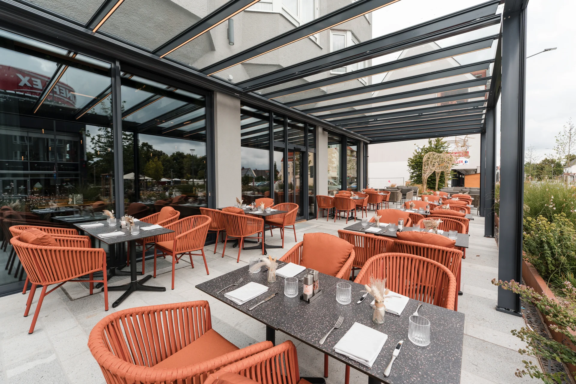 Außenbereich eines modernen Restaurants mit orangen Stühlen und überdachten Tischen