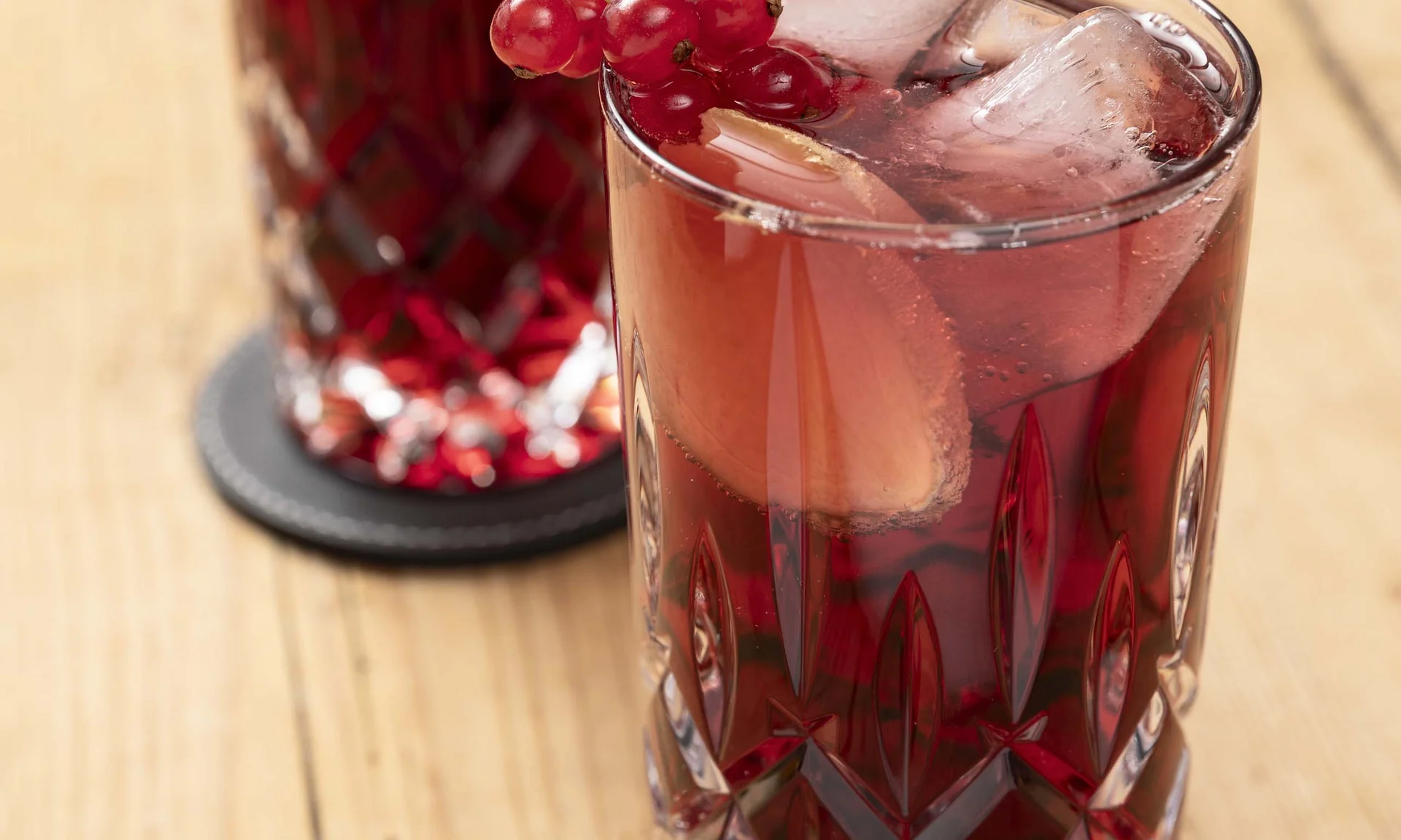Zwei Gläser mit rotem Getränk, Eis, rote Johannisbeeren und Zitrone auf Holzoberfläche