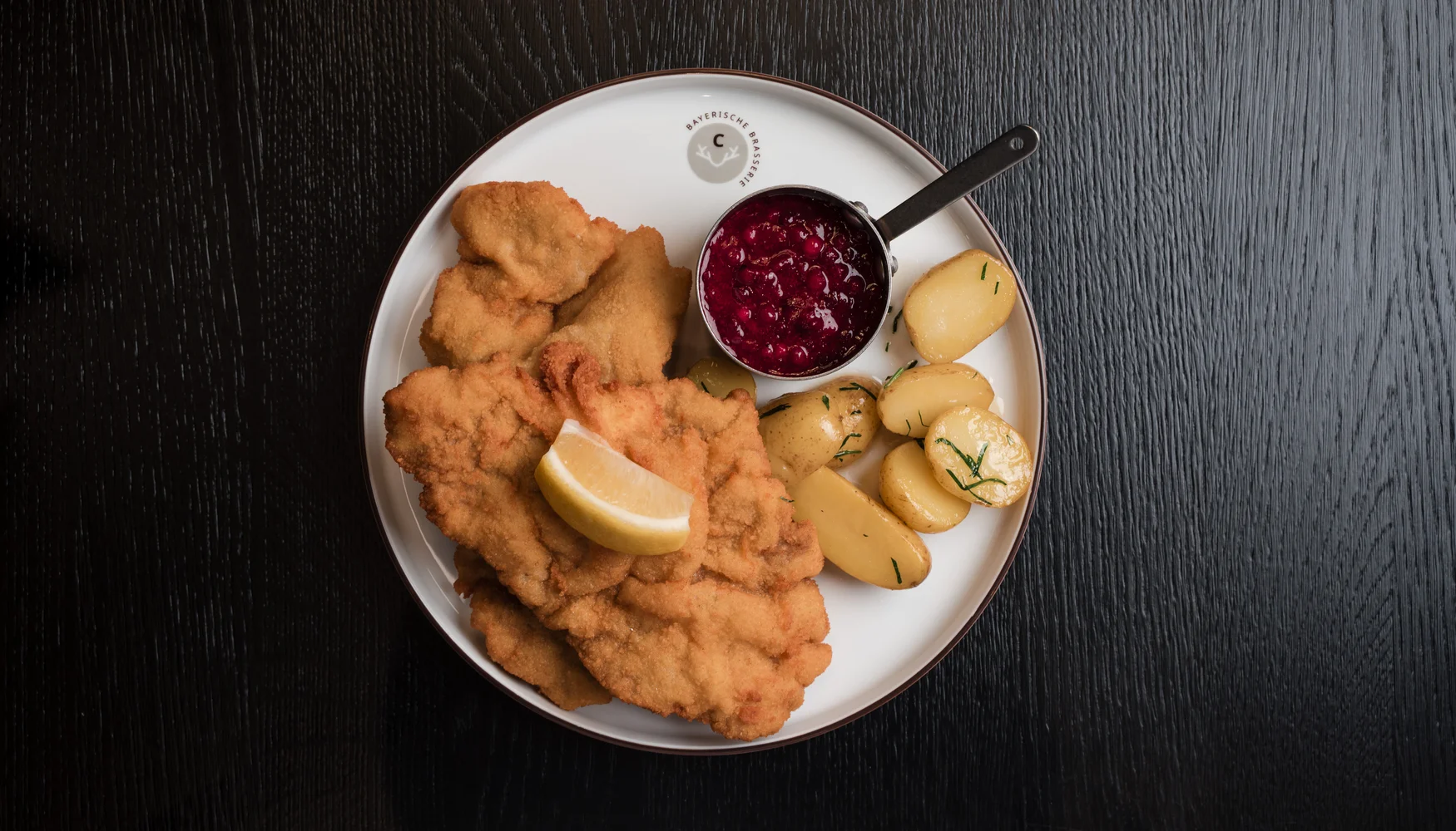 Unser Tipp: Abendessen im Cervus Wiener Schnitzel mit Kartoffeln, Preisselbeersoße und Zitronenscheibe auf weißem Teller