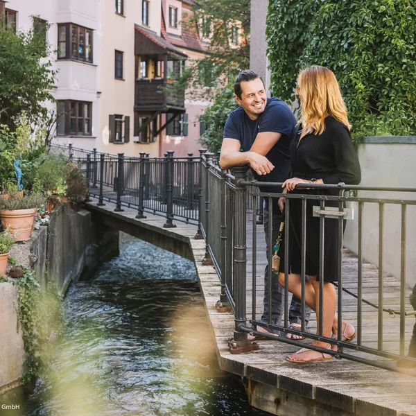 Zwei Personen unterhalten sich auf einer Brücke am Wasser in Augsburg.