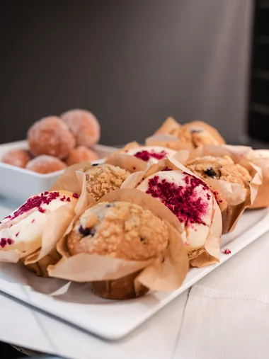 Kulinarik für Ihre Tagung Verschiedene Muffins auf einem weißen Teller mit Puderzuckerbällchen im Hintergrund