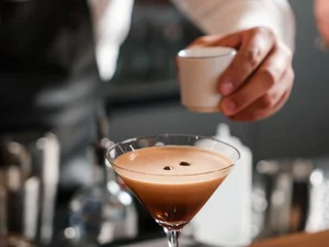Barkeeper dekoriert einen Cocktail mit Kaffeebohnen mit einer Pinzette