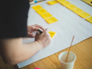 Person schreibt auf gelbe Haftnotizen auf einem weißen Blatt