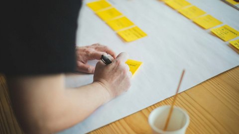Person schreibt auf gelbe Haftnotizen auf einem weißen Blatt