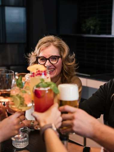Freundinnen stoßen mit bunten Cocktails und Bier in einer Bar an