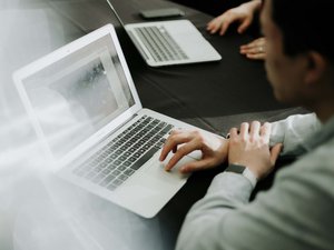 Person arbeitet an einem Laptop auf einem schwarzen Tisch mit zwei Laptops