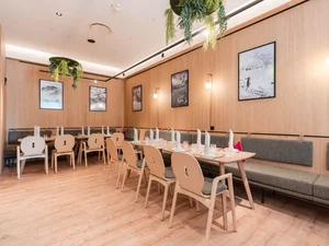 Südtiroler Stube Heller Gastraum im Restaurant Cervus mit gedeckten Holztischen, Sitzbänken, Holzstühlen, Wandbildern und Pflanzen.