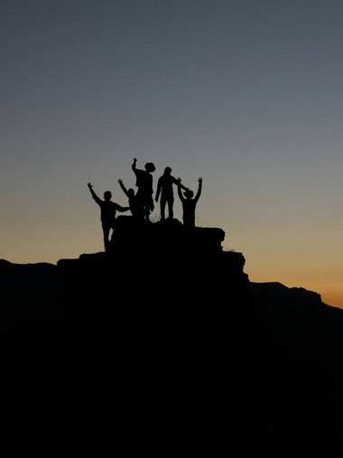 Silhouetten von fünf Personen auf einem Felsen bei Sonnenuntergang