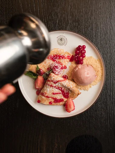 Hand bestreut Pfannkuchen mit Puderzucker und roten Beeren auf Teller