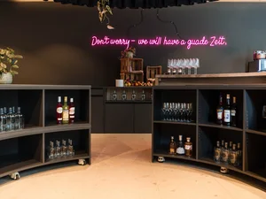 Zeller’s Quartier: das besondere Tagungshotel in Bayern Barbereich mit Regalen voller Flaschen und pinkem Neonlicht an der Wand