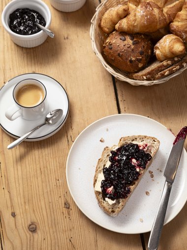 Frühstück mit Brot, Croissants, Butter, Marmelade und Espresso auf Holzuntergrund