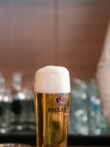 Ein Glas Paulaner Bier mit Schaum auf einem Bierdeckel auf der Bar