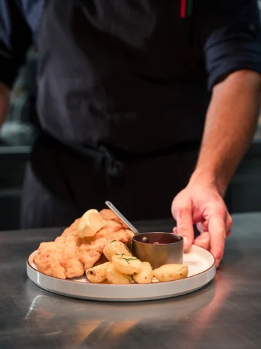 Koch serviert Wiener Schnitzel mit Kartoffeln und Sauce auf Teller