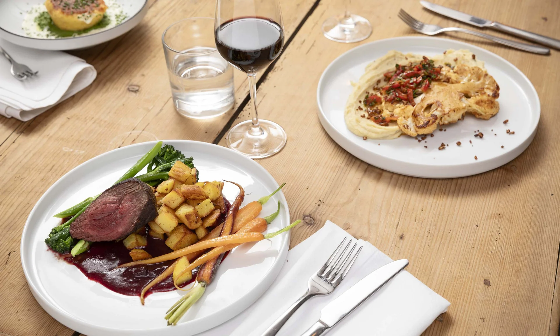 Drei Teller mit verschiedenen Gourmetgerichten und zwei Gläser, eines mit Rotwein