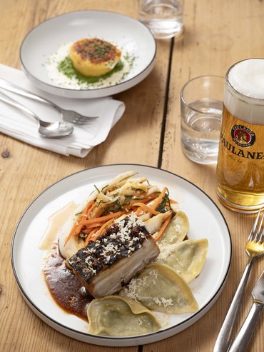 Plate with pork belly, vegetables, ravioli and a glass of beer on wooden table