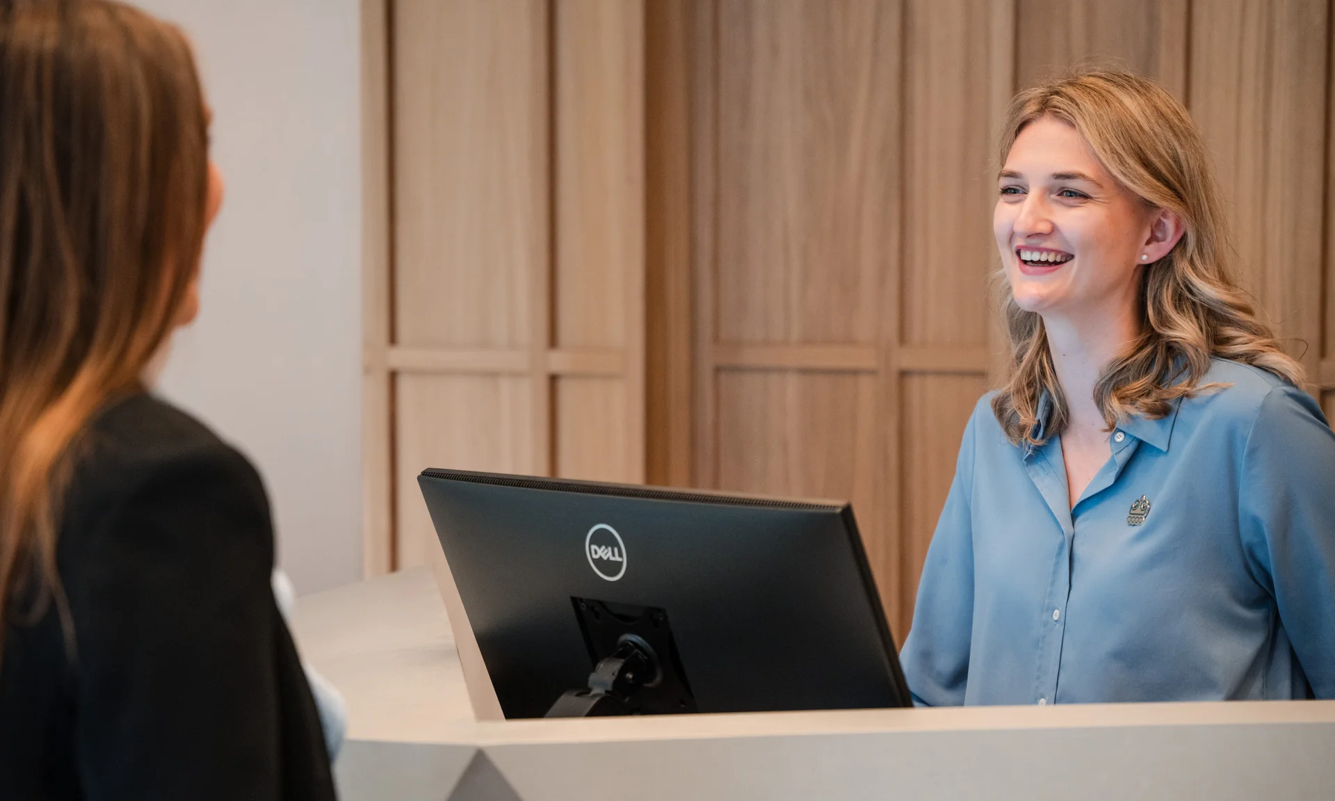 Lächelnde Empfangsfrau bedient Kundin am Schalter mit Computermonitor