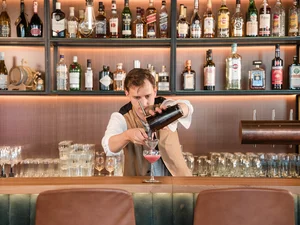 Barkeeper in der Cervus Bar Barkeeper mixt einen Cocktail hinter der Bar im Restaurant Cervus mit Spirituosenregal im Hintergrund.