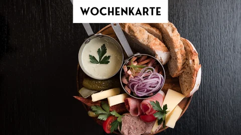 Brot, Aufschnitt, Käse und Dip auf Holzbrett vor Wochentafel