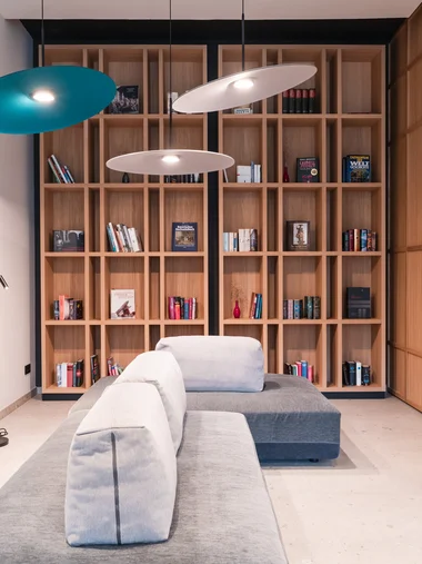 Moderner Wohnbereich mit grauem Sofa, Holzbücherregal und hängenden Lampen