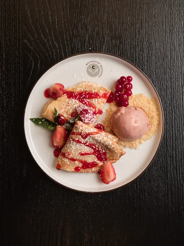 Ein dekorierter Crêpe mit Erdbeeren und einer Kugel Eis auf einem weißen Teller