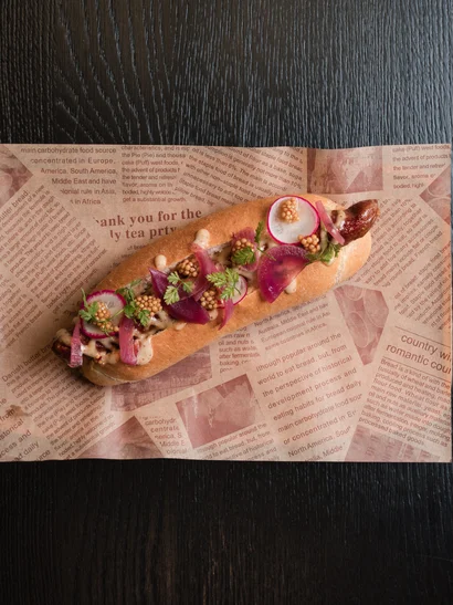 Cervus: das Restaurant in Königsbrunn mit dem gewissen Extra Gourmet-Hotdog mit Radieschen, eingelegten Zwiebeln, Senfkörnern und Kräutern auf Papier