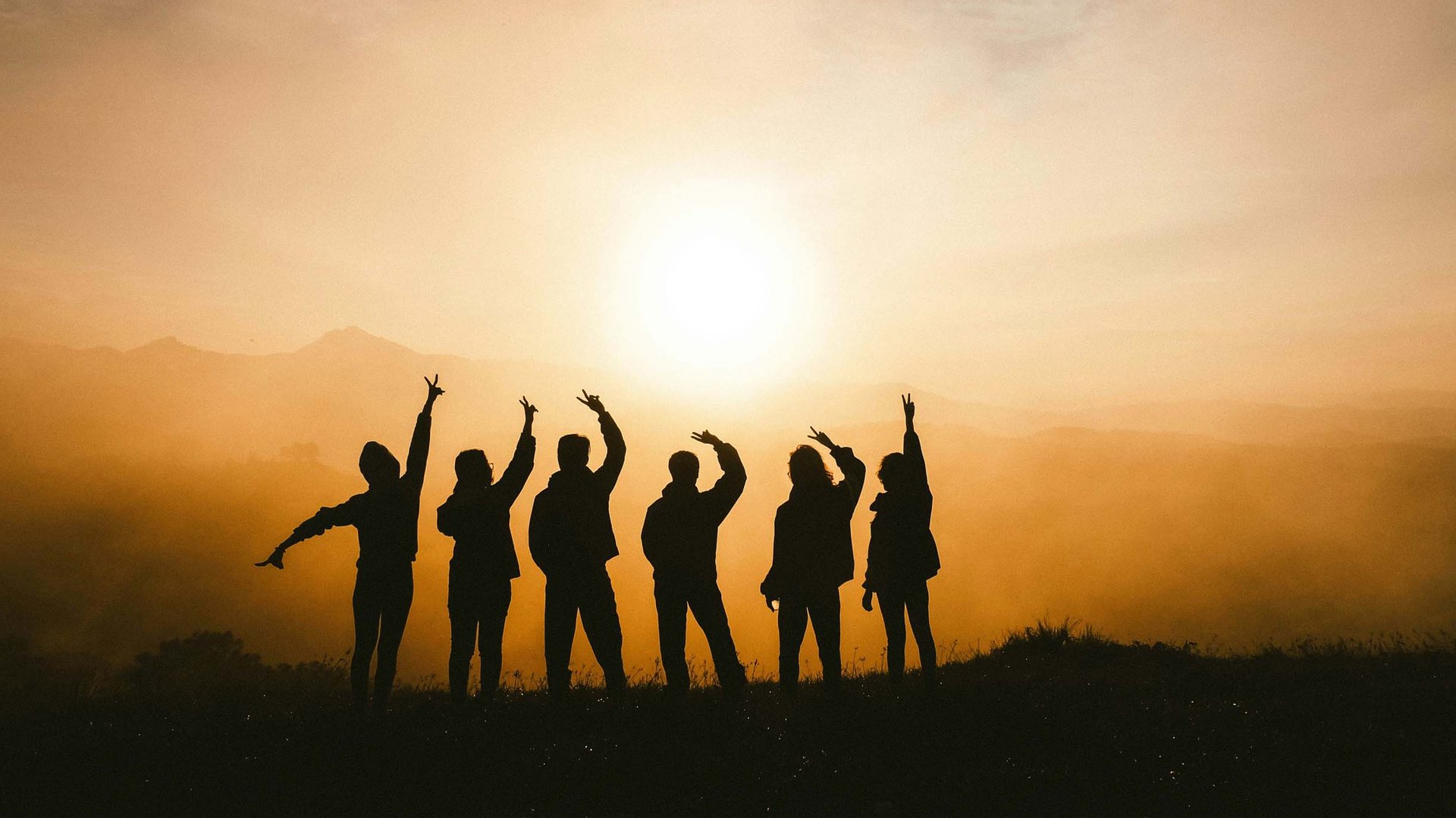 Gruppe von sechs Personen hebt Hände bei Sonnenuntergang in den Bergen