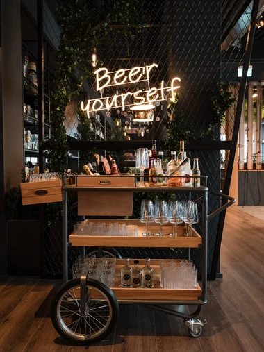 Getränkewagen mit Gläsern und Flaschen vor einem Neonzeichen Beer yourself
