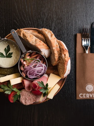 Speisekarte Brot, Käse, Aufschnitt, Zwiebeln und Soße auf einem Holzbrett, Besteck daneben