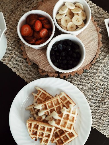 Waffeln auf Teller mit Schalen voll Erdbeeren, Bananen und Blaubeeren